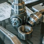 Various metal mechanical parts and blueprints on a mesh table.